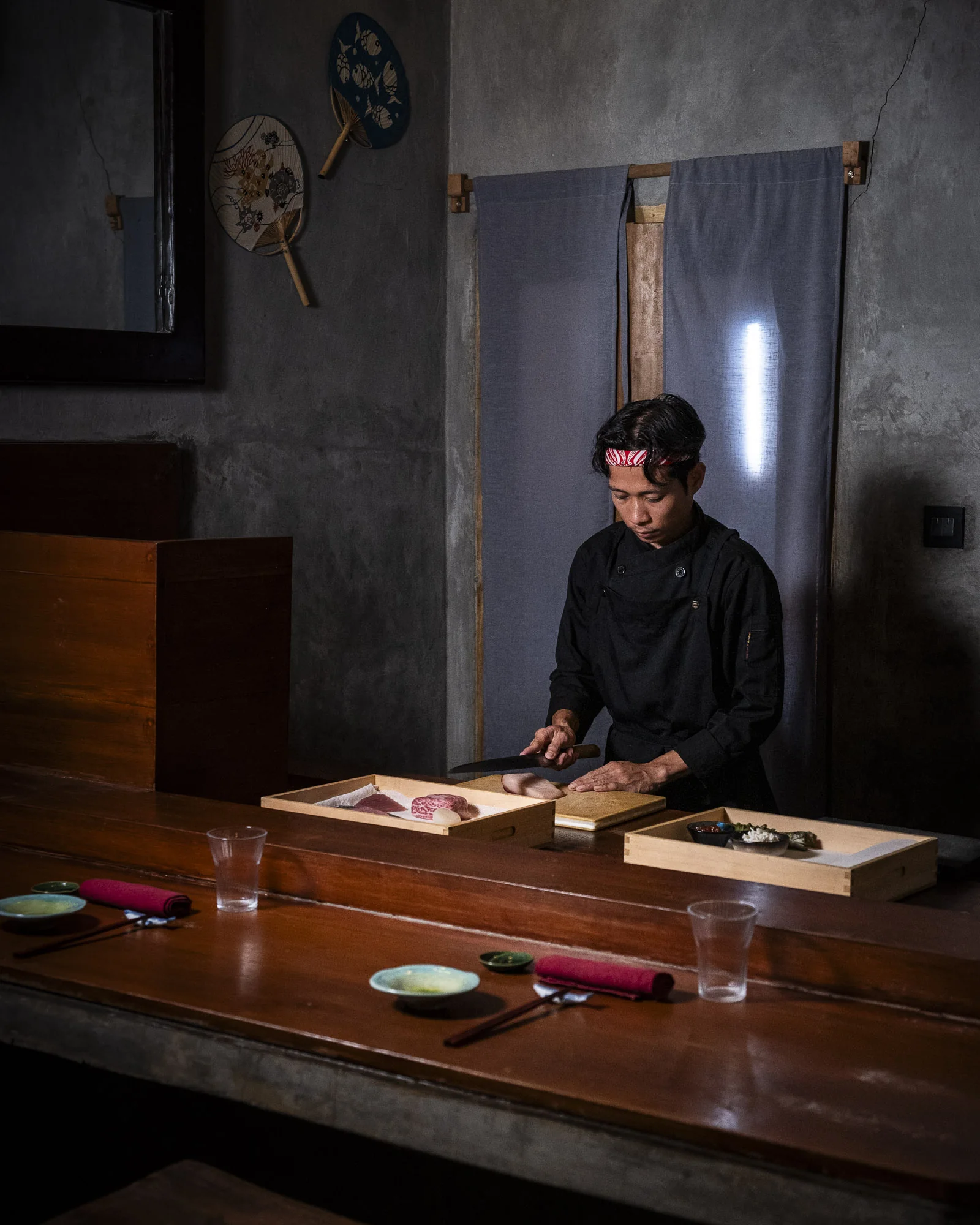 The chef at the counter, knife in hand, preparing fish in front of two guest place settings